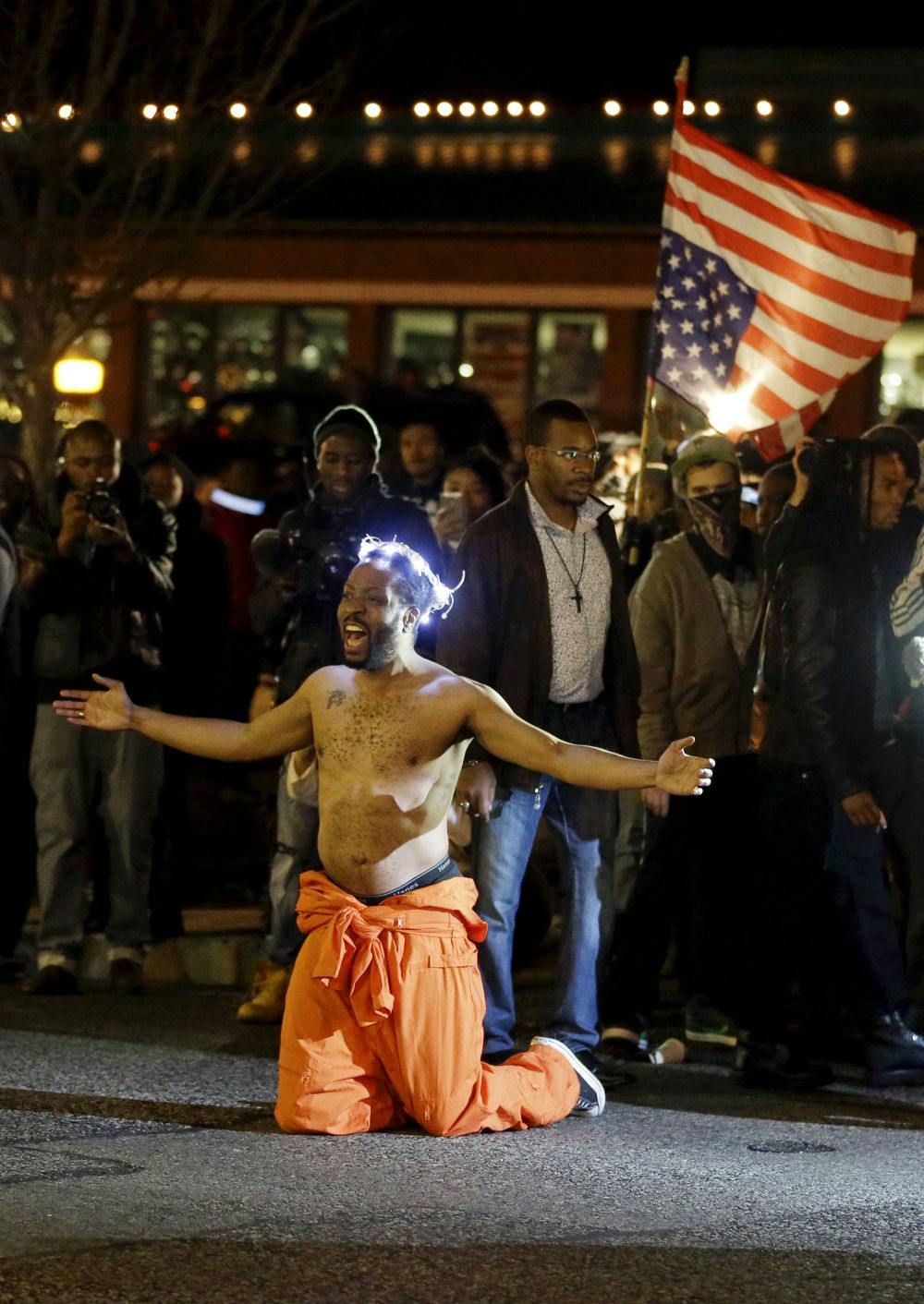 A man kneels in the middle of a street and yells at police before being arrested outside the Ferguson Police Department Saturday, Nov. 29, 2014, in Ferguson, Mo. (AP Photo/Jeff Roberson)