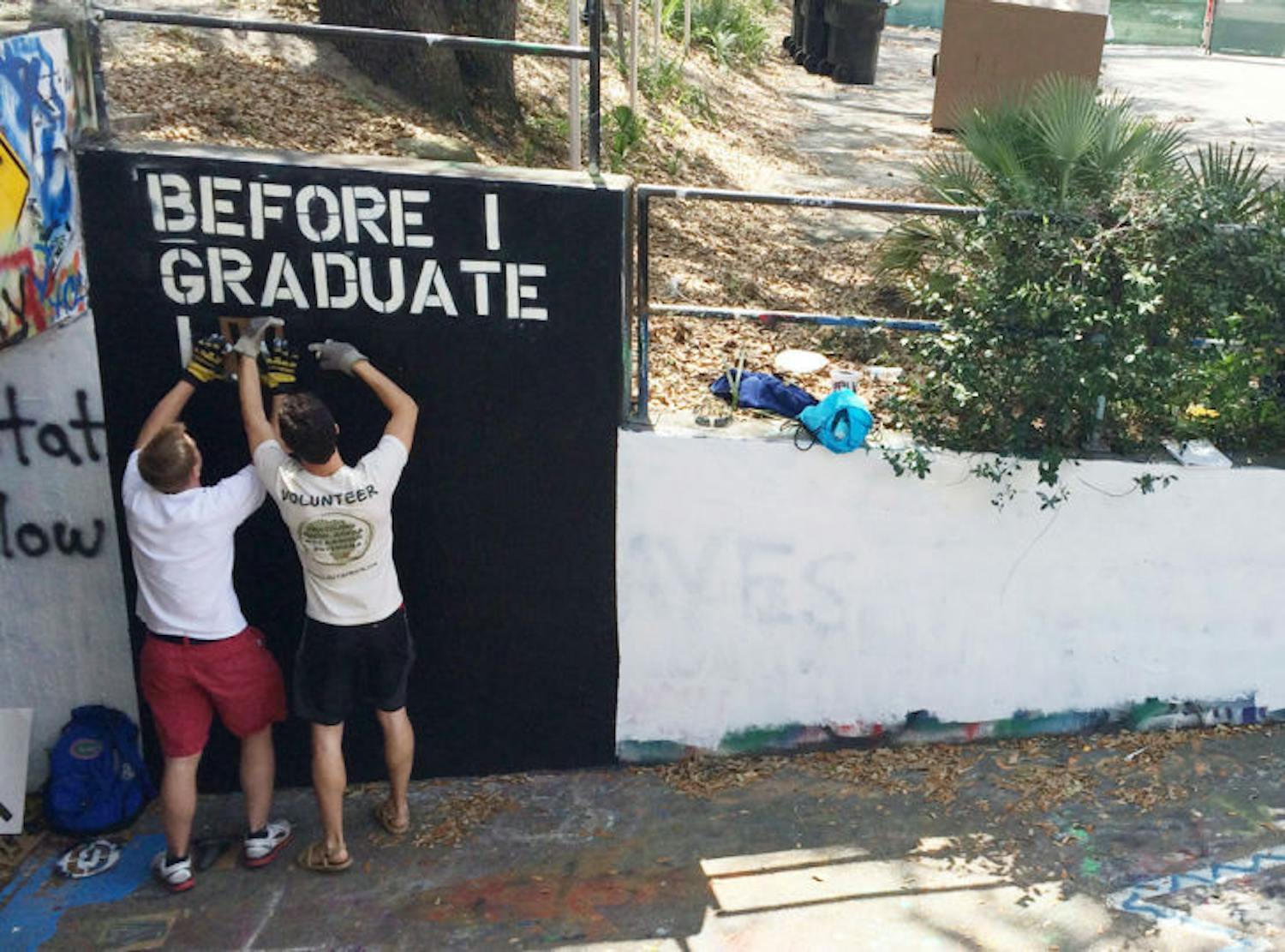 Danny Fry and Tyler Burris, president and treasurer of Humons respectively, spray paint individual stencil letters white onto a black background in the recently repainted Norman Hall tunnel. Humons is a student organization that promotes humans learning to live as one.