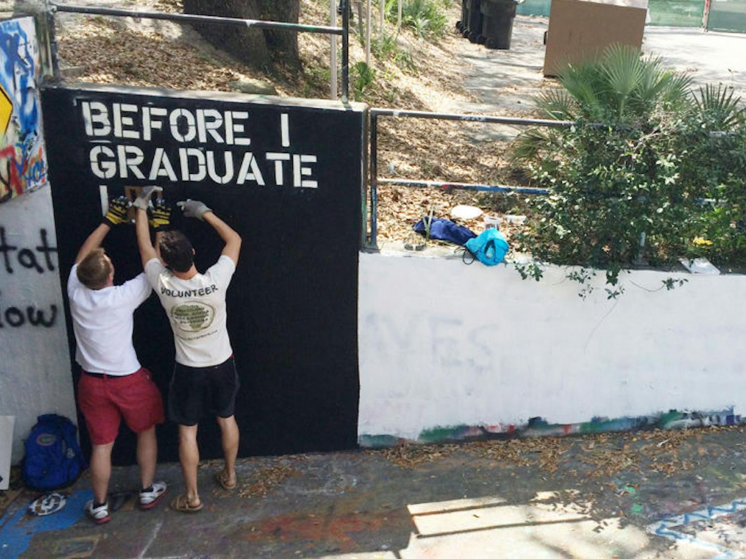 Danny Fry and Tyler Burris, president and treasurer of Humons respectively, spray paint individual stencil letters white onto a black background in the recently repainted Norman Hall tunnel. Humons is a student organization that promotes humans learning to live as one.
