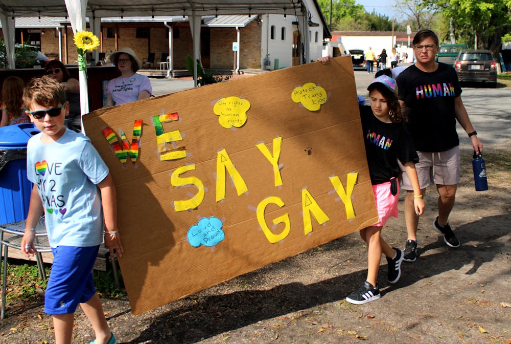 Becky Fields, a teacher at Talbot Elementary School, and Fields' two children hold a "We Say Gay" sign to protest Florida's Don't Say Gay bill at Heartwood Soundstage on Saturday, March 19. The bill has passed the state legislature and is on the governor's desk.