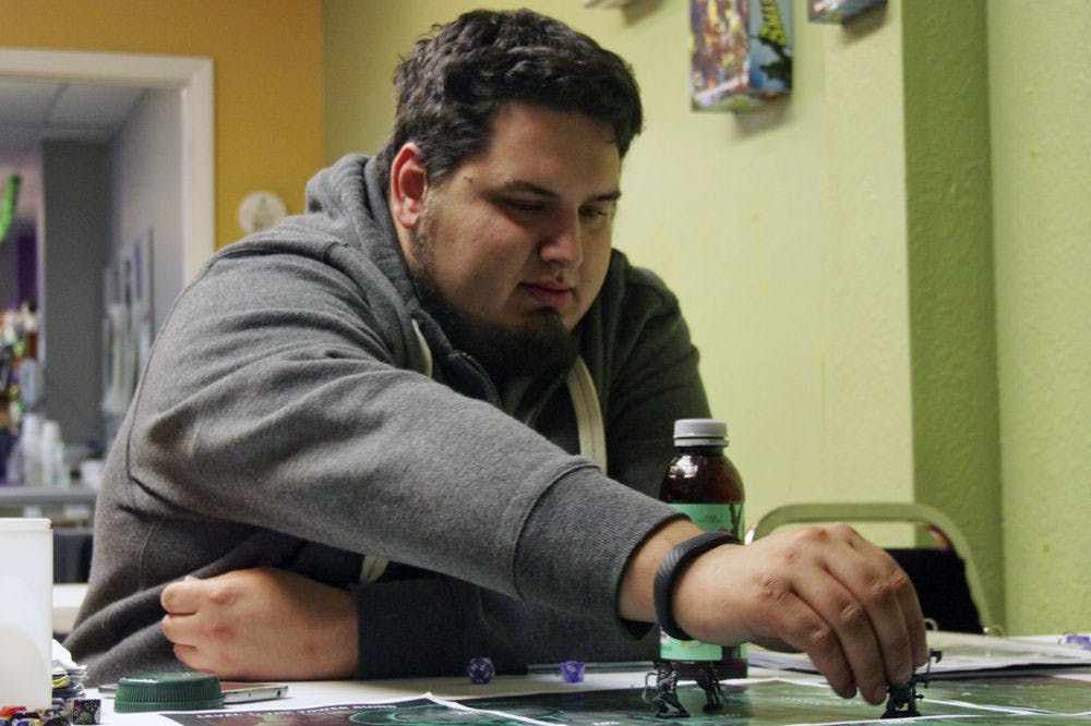 Robert Kagel, a 21-year-old UF information systems senior, reaches across the table to move a game-piece representing his in-game character, Kahw the Tengu. Kagel was playing a campaign from the table-top game Pathfinders, in which players adopt personas and play through dungeons represented by table mats.
