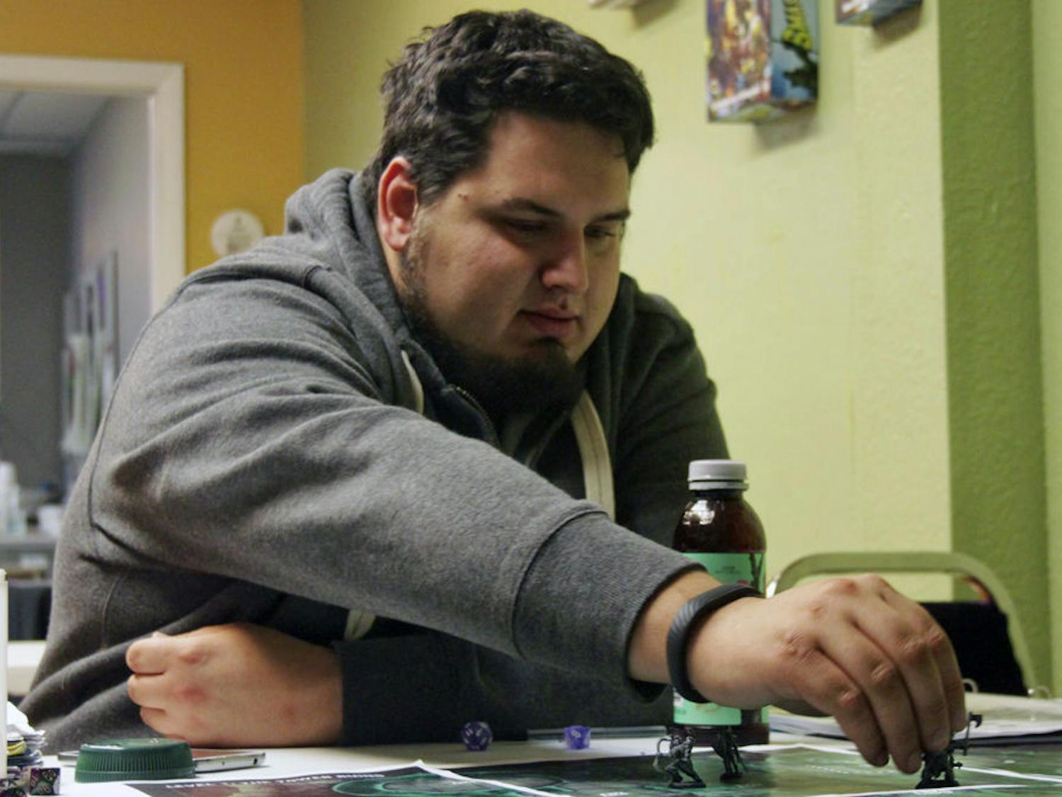 Robert Kagel, a 21-year-old UF information systems senior, reaches across the table to move a game-piece representing his in-game character, Kahw the Tengu. Kagel was playing a campaign from the table-top game Pathfinders, in which players adopt personas and play through dungeons represented by table mats.