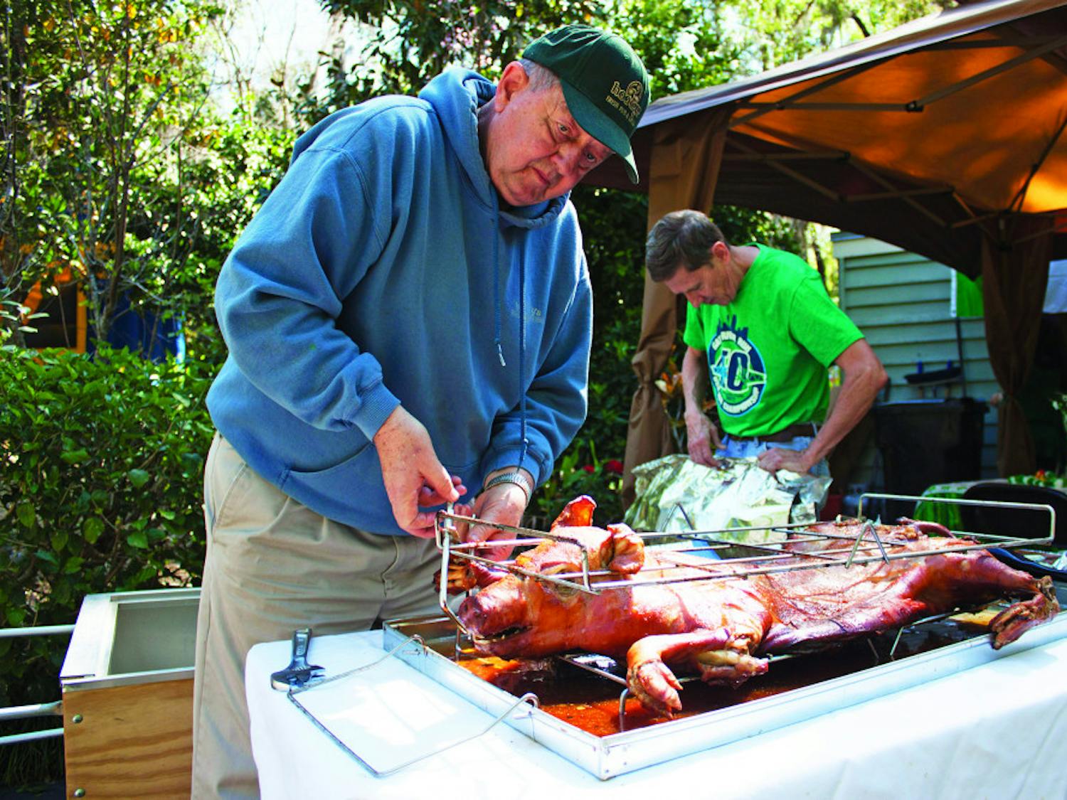 Larry King, 76, loosens a rack holding a roasted pig as Jim Ferrer, 66, makes a tent out of aluminum foil to keep it warm for a day-after-St. Patrick's Day party at the corner of Northwest 14th Avenue and Northwest 18th Street on Saturday. King and Ferrer roasted the pig for about four hours before serving it. 