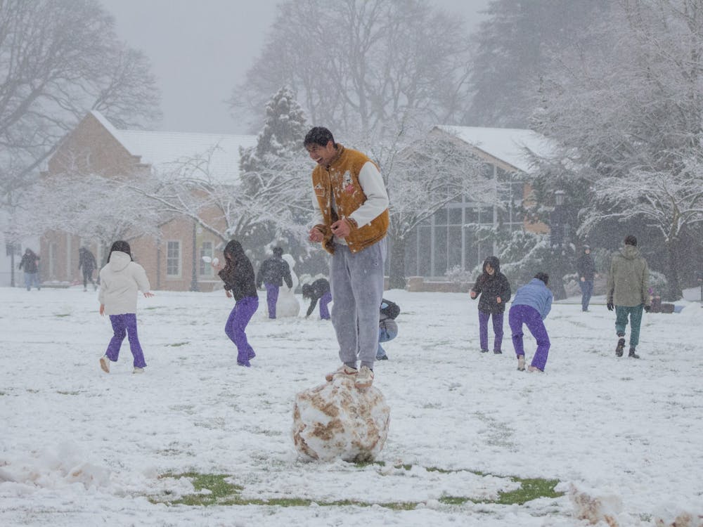 A student stands on top of their rolled snowball amidst nursing majors collecting snow in the quad in front of the Clark Library and Franz campus. Photo by