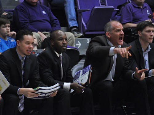  The coaches sit on the bench during a game. Assistant coach Eric Jackson (second from the left) has been coaching at UP for nine seasons. | Photo by Kristen Garcia