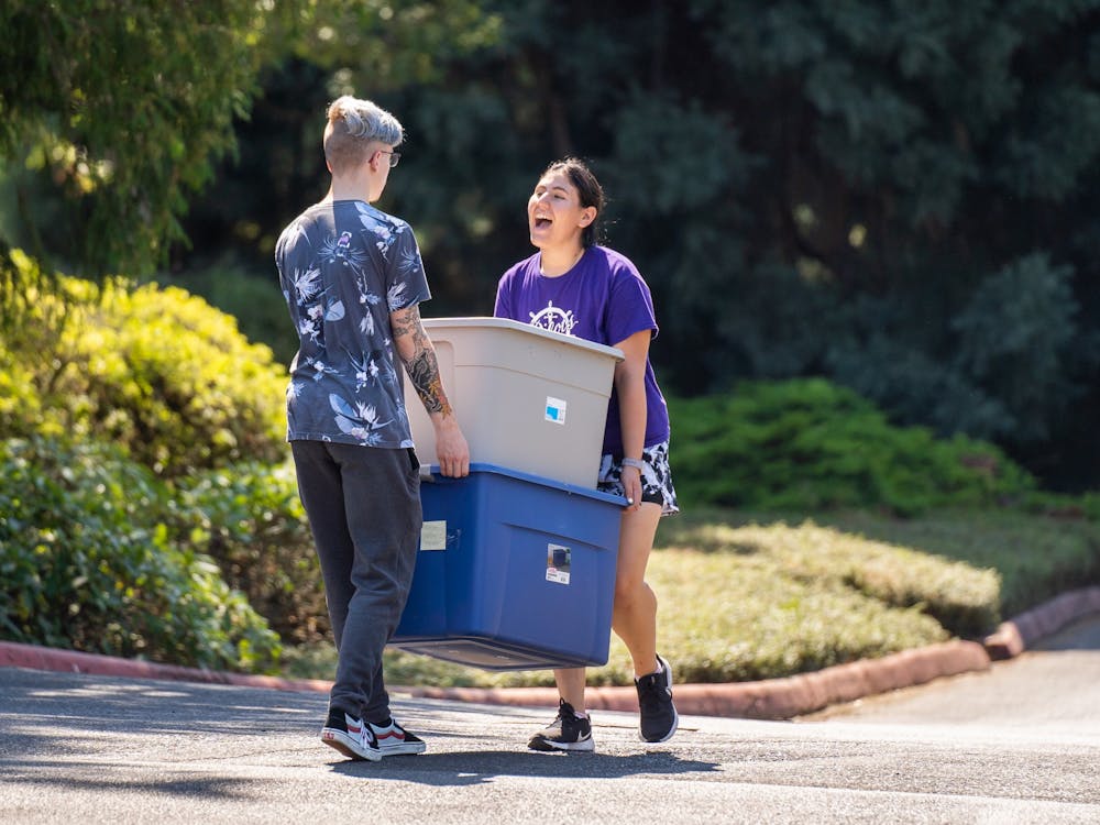 Two people carry bins through the main parking lot.