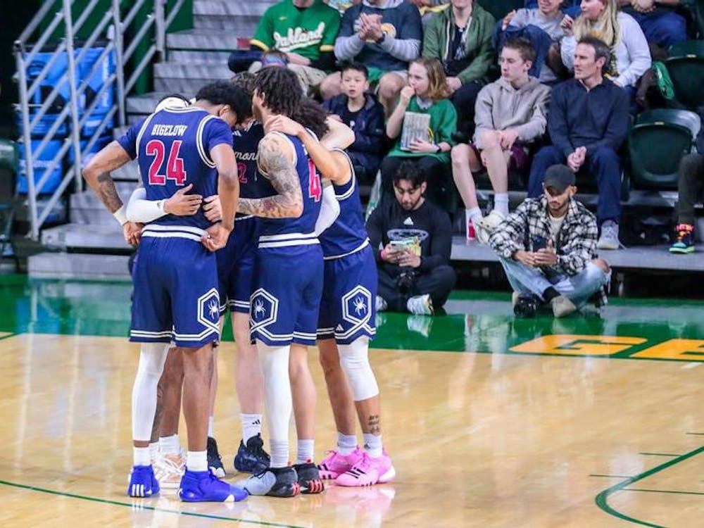 Graduate forward Isaiah Bigelow and senior guard Dji Bailey confer with teammates during the March 9 game against George Mason University. Courtesy of Richmond Athletics.
