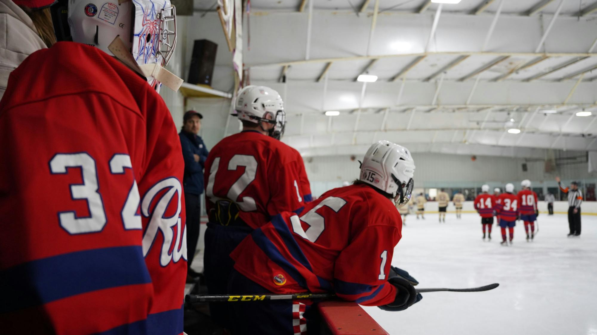 UR club ice hockey players look out at the ice rink from their bench.