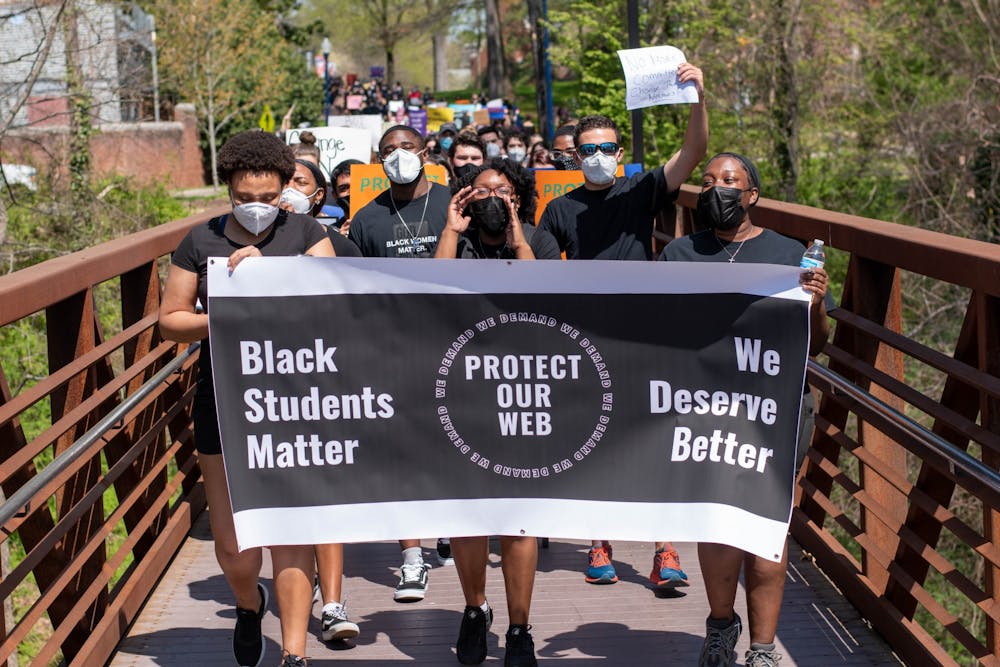 <p>Protesters march across the bridge leading into parking lot U21. Leaders of the protest carry a Protect Our Web banner that reads "Black Students Matter" and "We Deserve Better."</p>