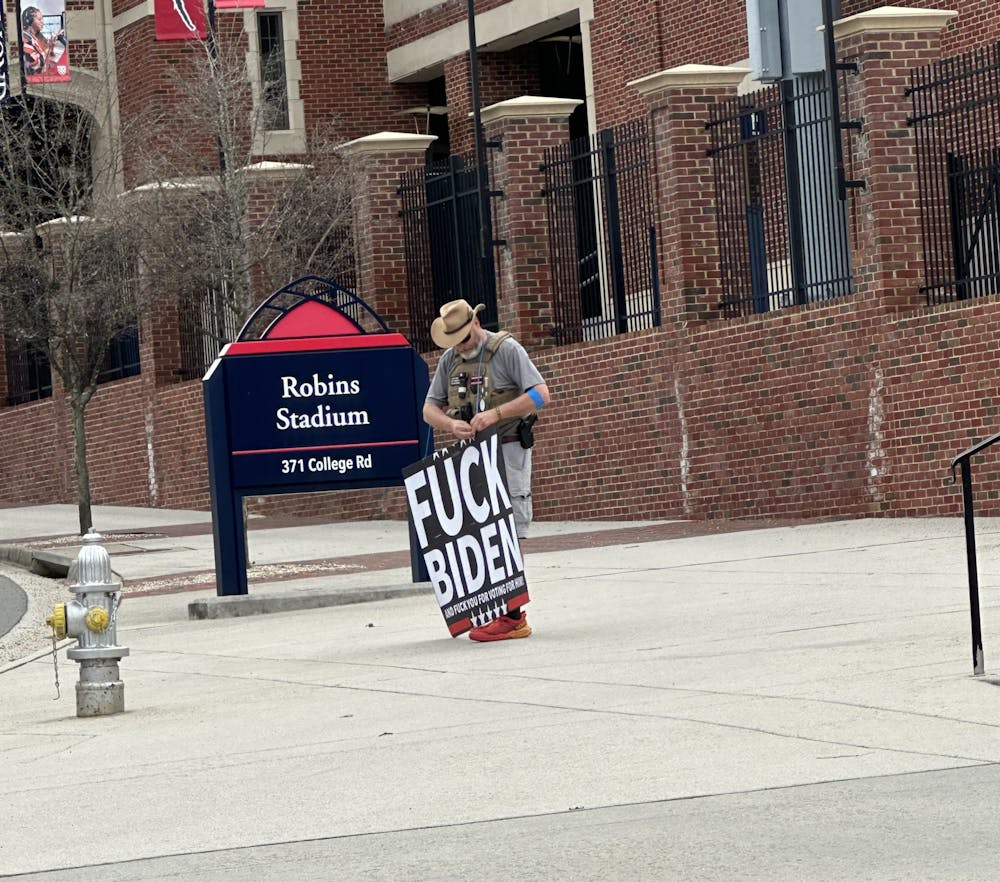 <p>Ron Hedlund, armed and holding a poster reading "Fuck Biden", stands outside the Robins Center Jan. 10.&nbsp;</p>