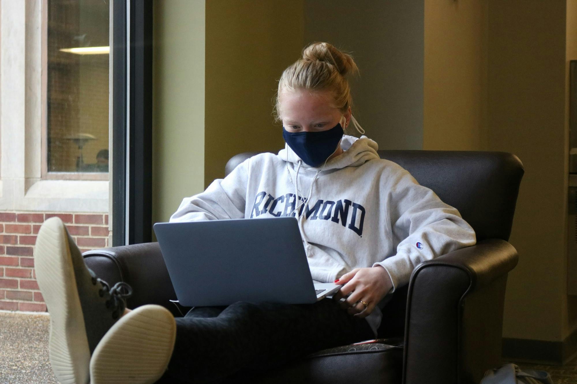 A masked student sits with a laptop in Boatwright Memorial Library.