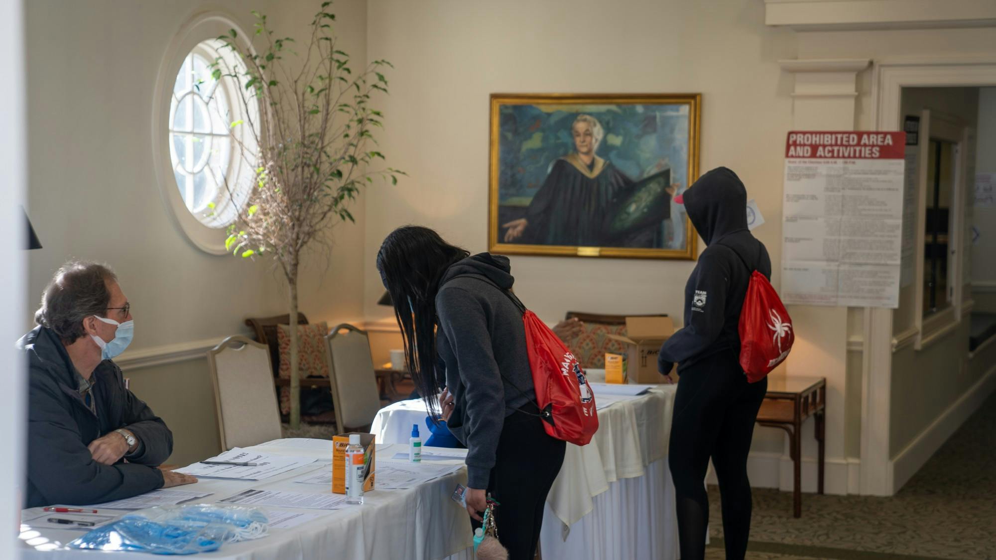 Two student-athletes sign in to vote among hand sanitizer, masks and COVID.
