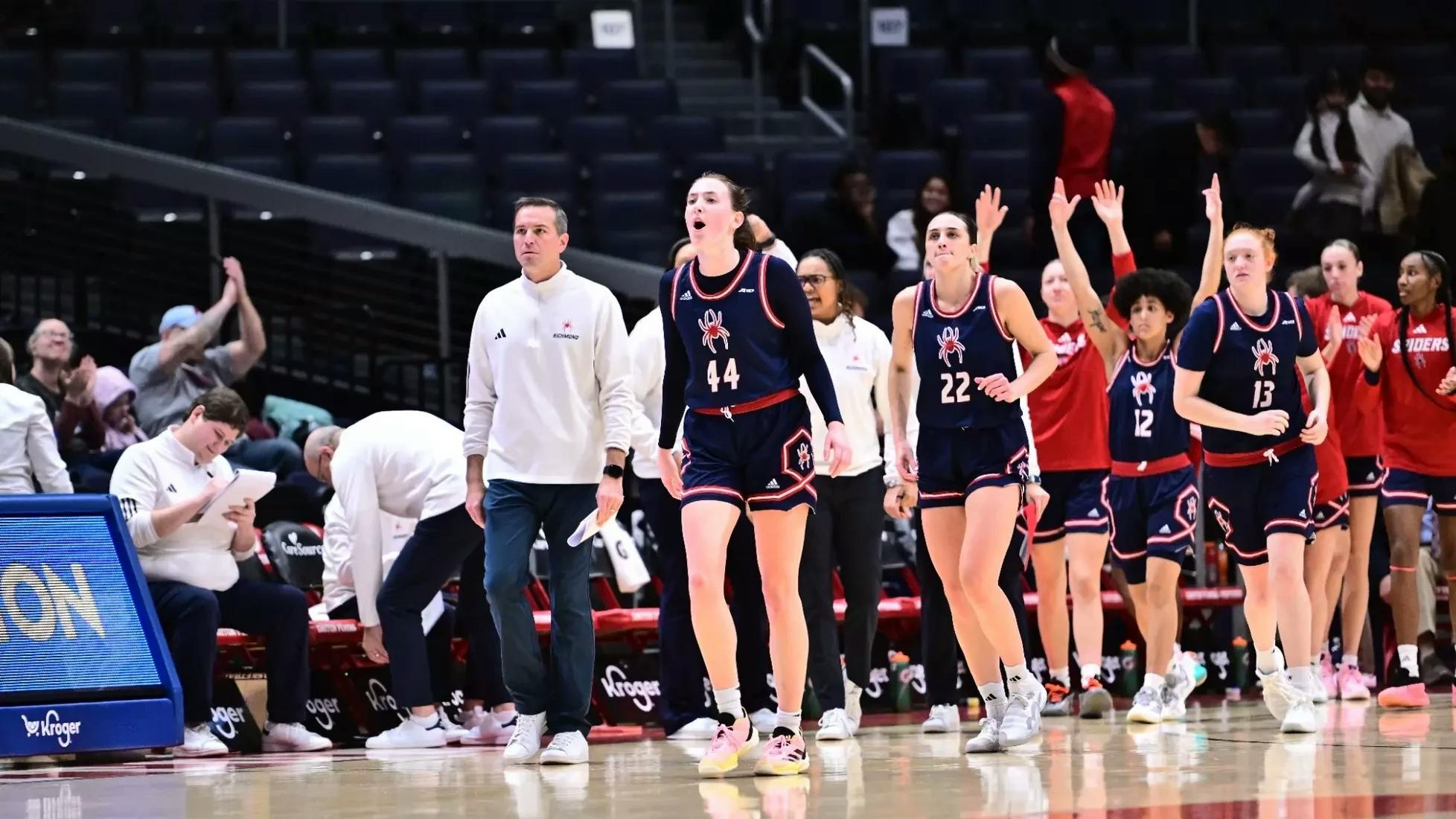 The Spiders Women's Basketball Team with junior forward Maggie Doogan cheering in front. Courtesy of Richmond Athletics.