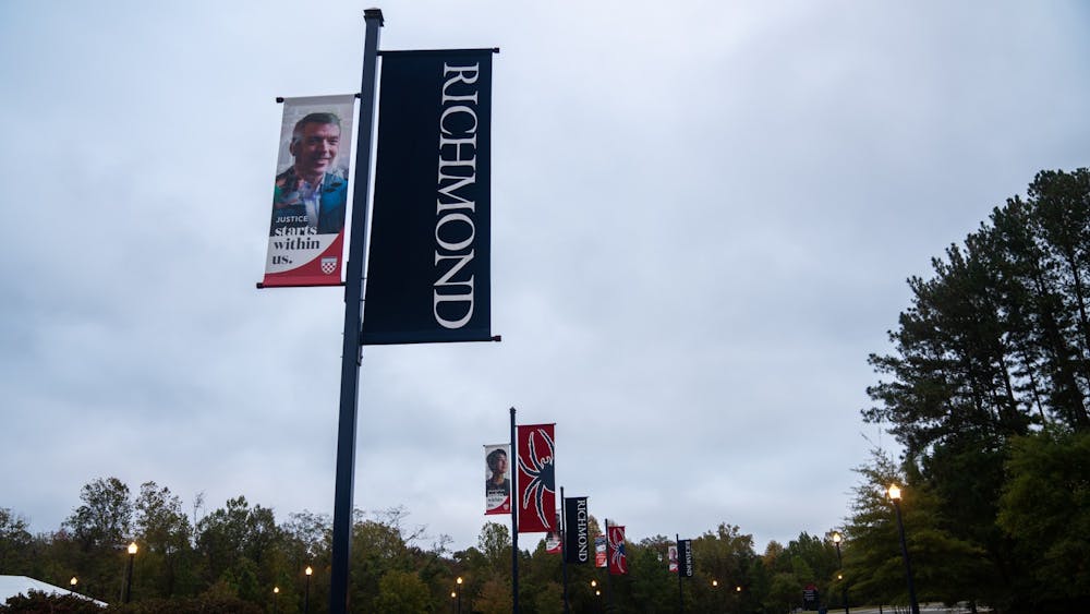 University signs hung beside the River Road entrance glisten in the glow of the street lamps on a cloudy night.