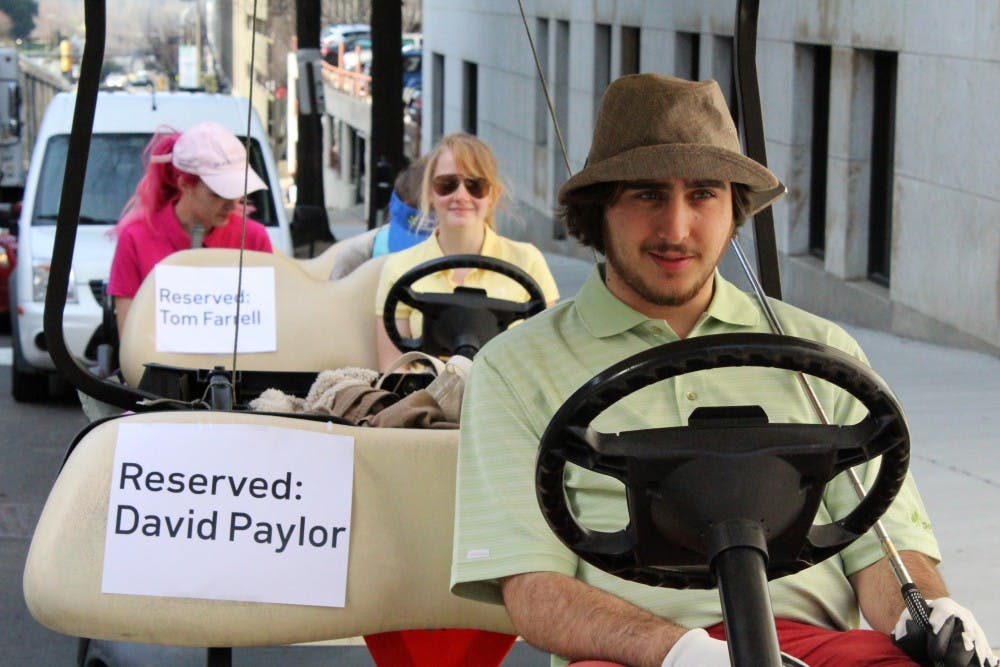 Michael James-Deramo, chair of the VCU chapter of the Virginia Student Environmental Coalition, sits in a golf cart meant to represent the Masters tournament trip gifted to David Paylor by Dominion in 2013.