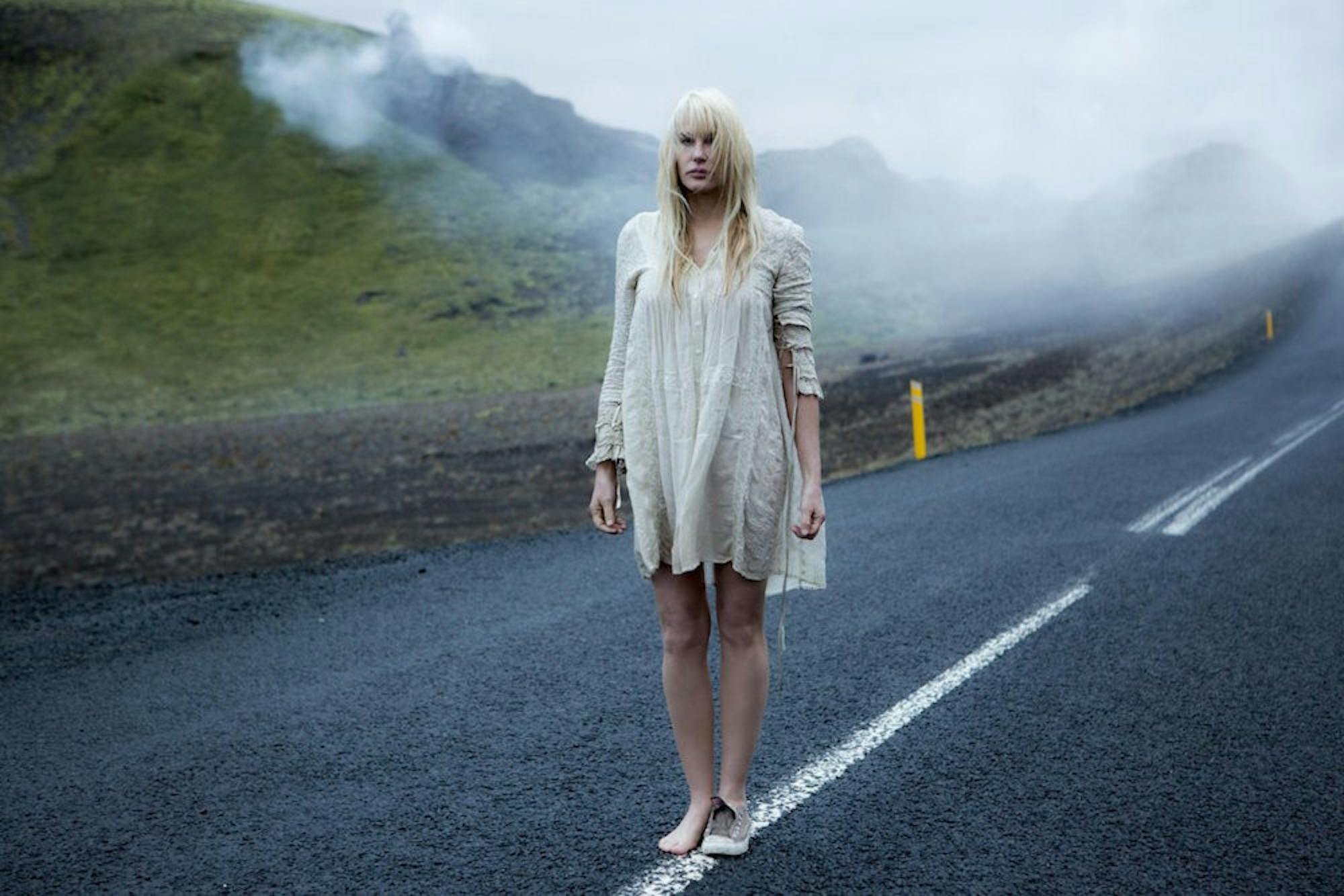 Daryl Hannah plays a mysterious woman in a white shift dress who continuously appears to the eight strangers. / Courtesy of Netflix