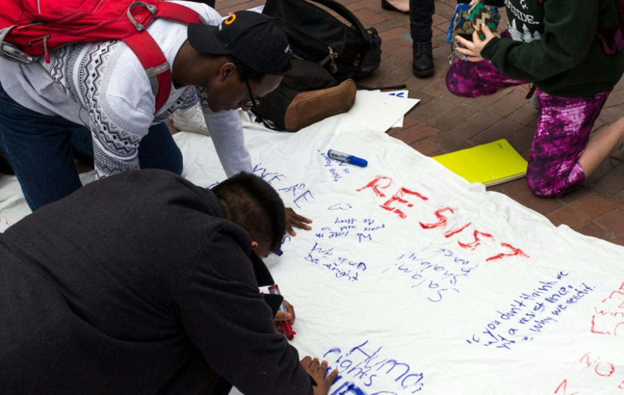 College senior Dennis Kamara (top) and College senior Harpreet Singh (bottom) sign march organizer and College freshman Ruhika Prasad's bed sheet. / Matthew Hammond, Staff