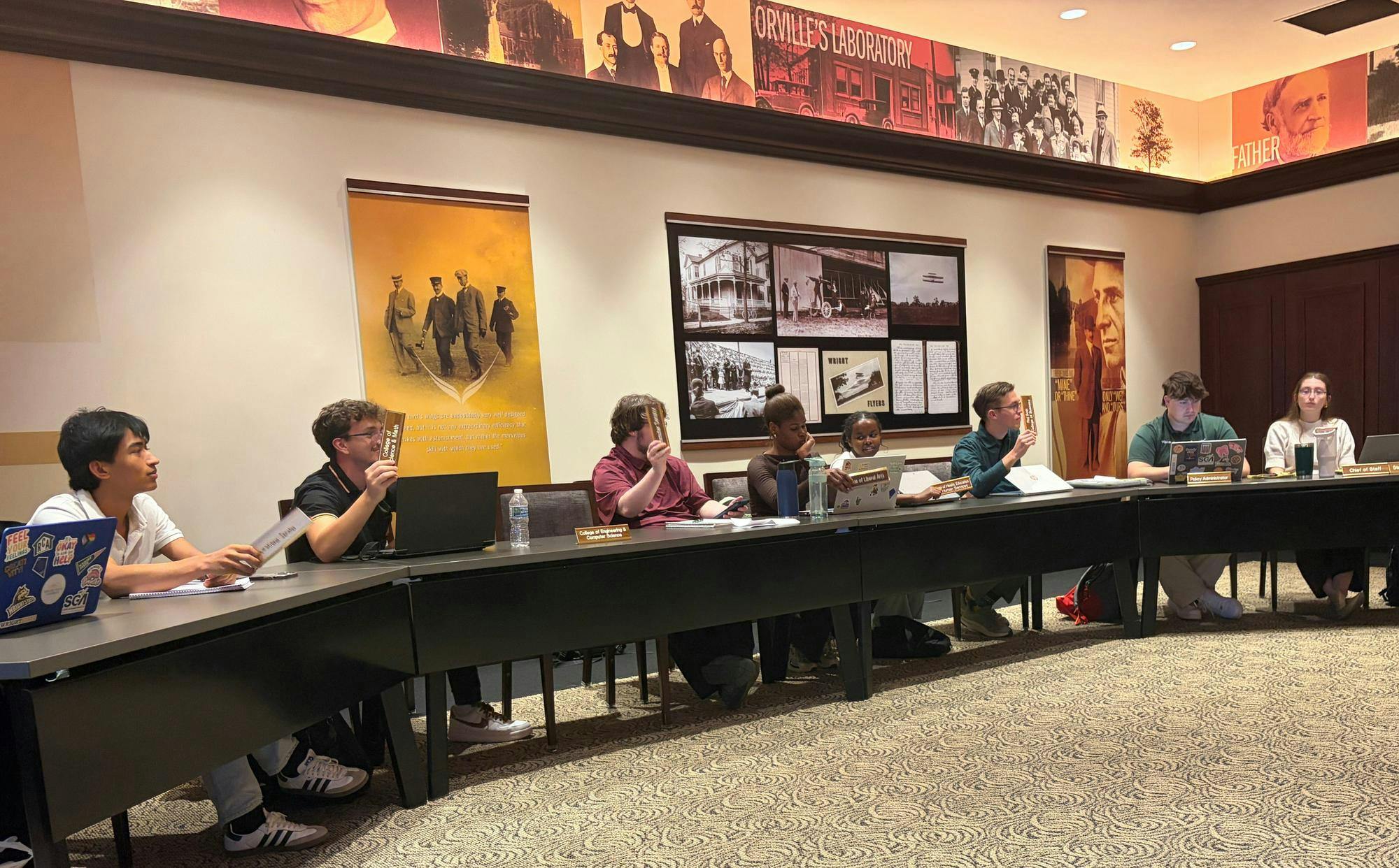 SGA sitting at a table, holding up nametags 